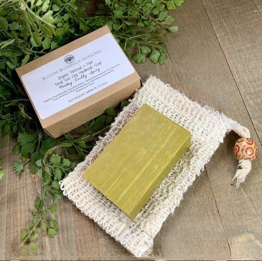 Handmade Patchouli, Mint and Dead Sea Clay Soap placed on a free Ramie drawstring soap saver bag. All displayed on a pretty wooden background with green leaves. This soap smells so good.